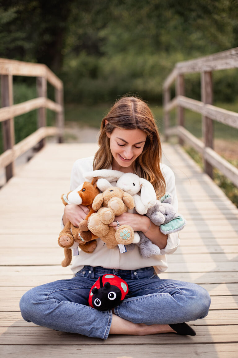 heather levine founder of maxie plush and luckables sitting on a bridge holding plush stuff animals.